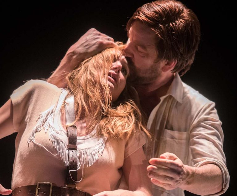 Twee acteurs in een dramatische scène waarbij een man een vrouw kust terwijl zij in zijn armen leunt.