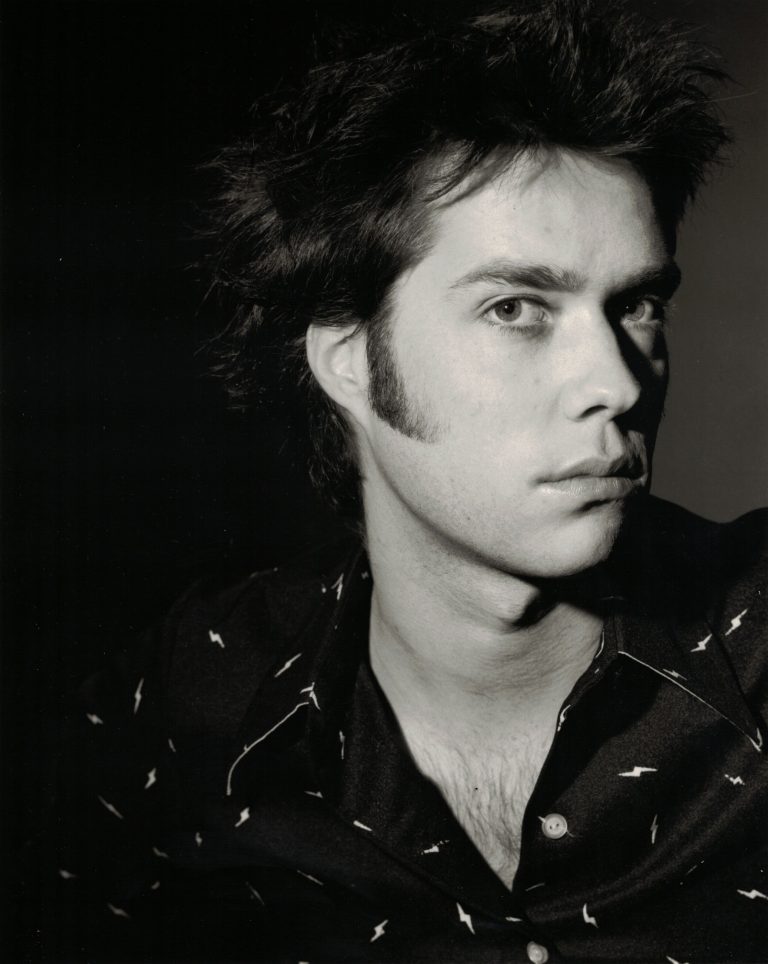 Zwart-witportret van een man met een edgy kapsel en een ingetogen uitstraling.