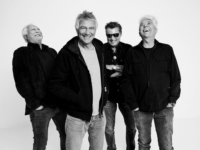 Zwart-wit afbeelding van vier mannen die lachend poseren in casual kleding.