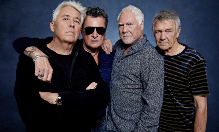 Een groep van vier oudere mannen poseert samen voor een neutrale achtergrond.