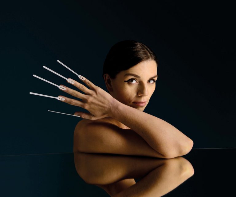 Een vrouw met lange, opvallende nagels poseert tegen een donkere achtergrond.