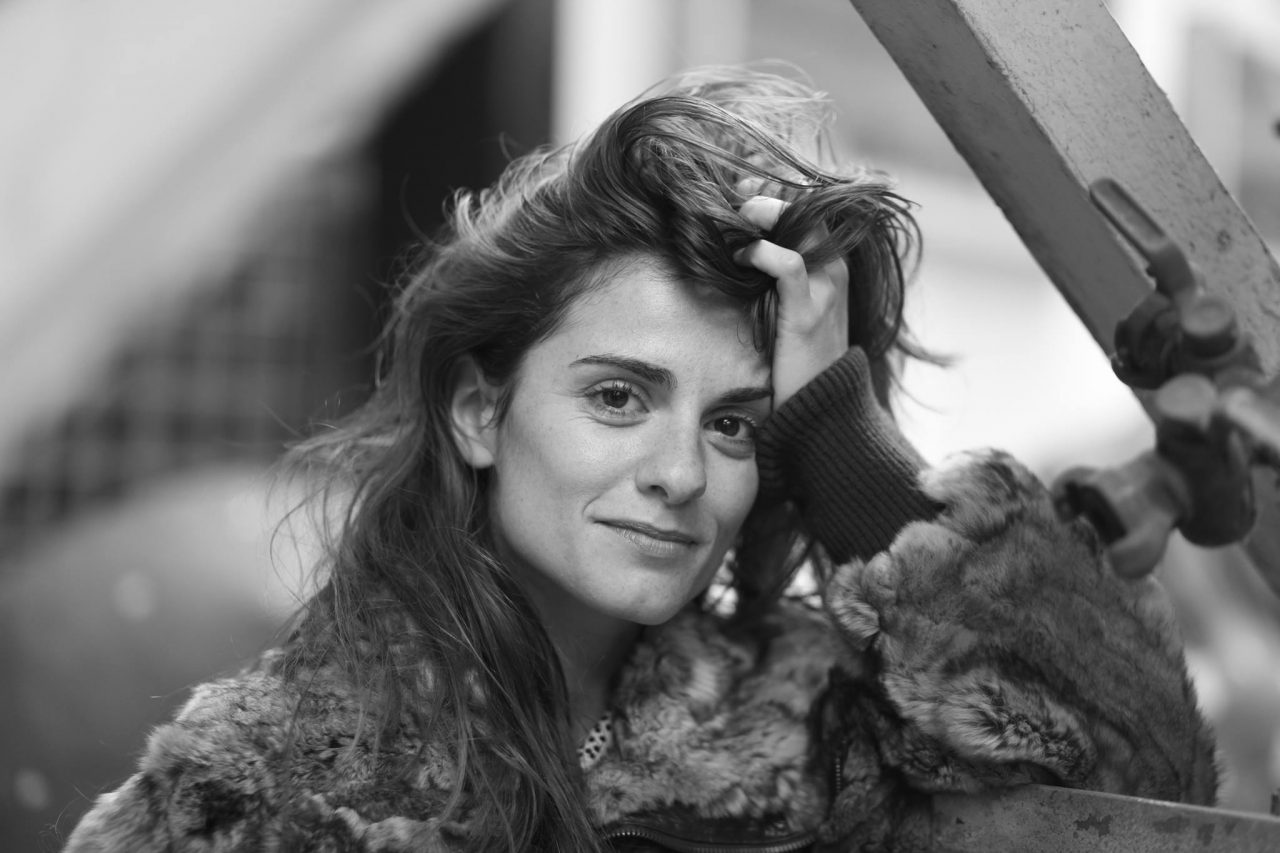 Zwart-witportret van een vrouw met lang, golvend haar, die haar hand door haar haar haalt en naar de camera kijkt.