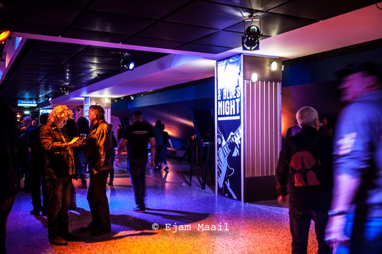 In een kleurrijk verlichte zaal staan mensen te socializen en te genieten van een evenement.