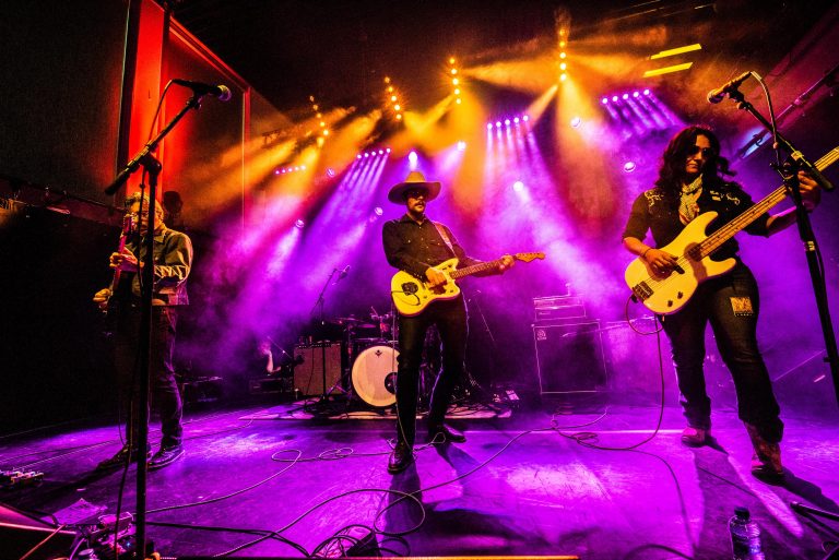 Een band speelt op een podium met kleurrijke lichten en damp.