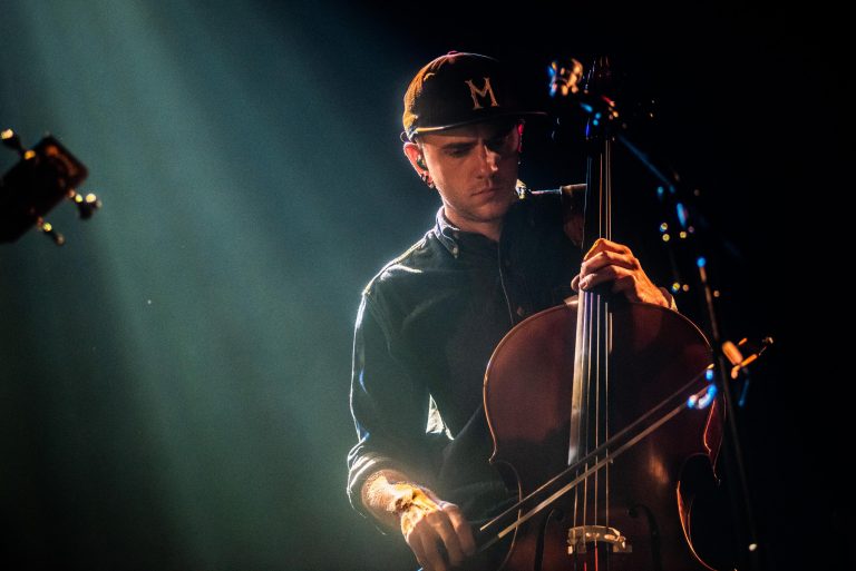 Een muzikant speelt cello op een podium, verlicht door opvallend licht.