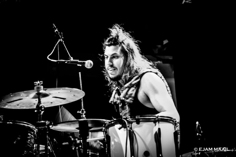 Een drummer in een zwart-wit setting, energiek aan het spelen achter zijn drumstel.