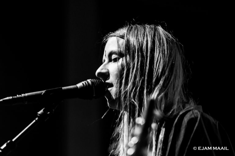 Een persoon zingt in een microfoon met een serieuze expressie, gefotografeerd in zwart-wit.