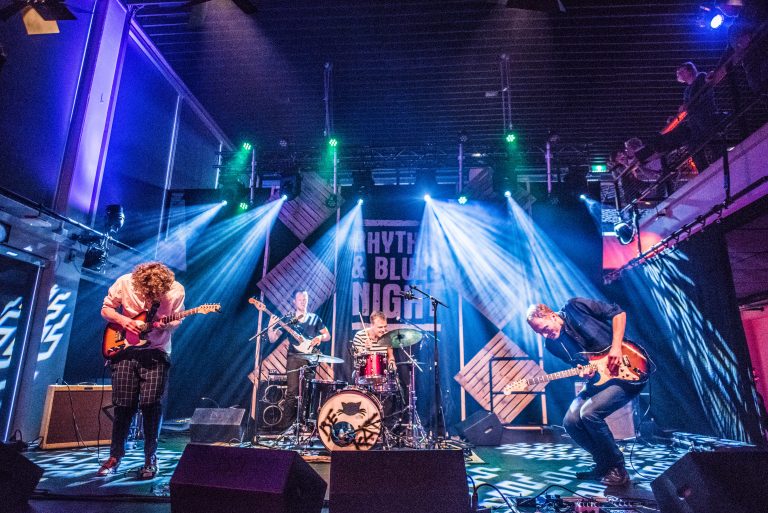 Een band performt op een podium met kleurrijke lichten en een energieke sfeer.