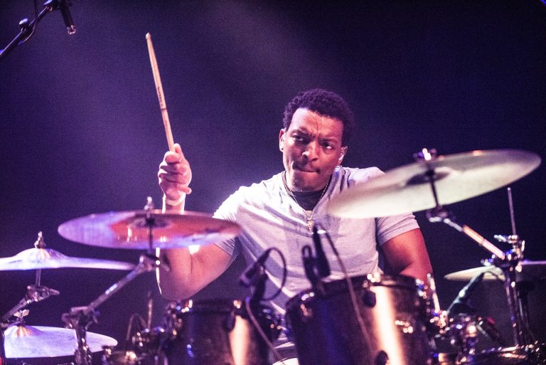 Een man zeer gefocust aan het drummen met in zijn ene hand een drumstok