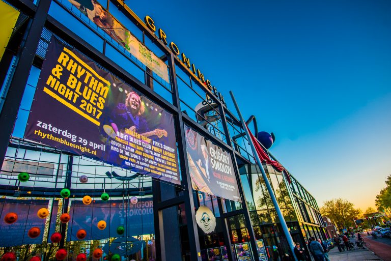 Gevel van een gebouw met opvallende affiches voor een muziekevenement en helder blauwe lucht.