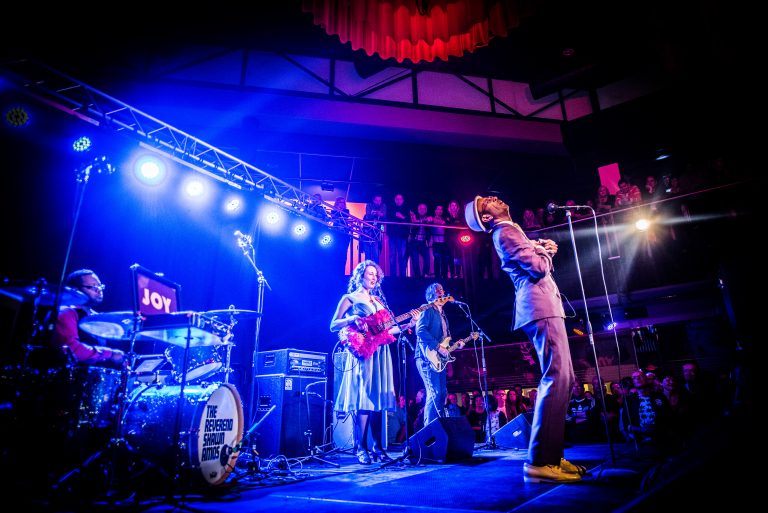 Een liveband presteert op een podium met kleurrijke verlichting en enthousiaste muziek.