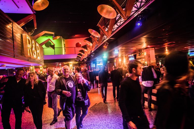 Een drukke nachtclub met kleurrijke verlichting en mensen die door de ruimte lopen.