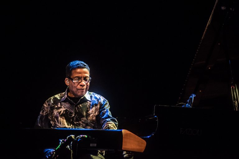 Een muzikant speelt piano op een podium met een donkere achtergrond.