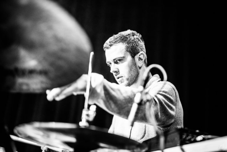 Een drummer speelt geconcentreerd op zijn drums tijdens een live optreden.