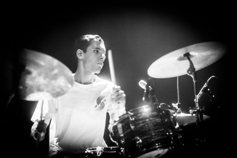 Drummer in actie, met een geconcentreerde uitstraling terwijl hij op een drumstel speelt.