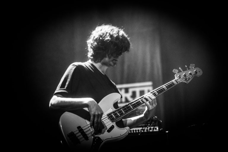 Een muzikant speelt basgitaar op een podium in zwart-wit.