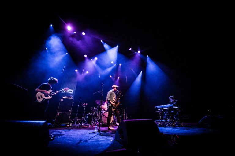 Een band performt op een podium, omringd door kleurrijke verlichting.