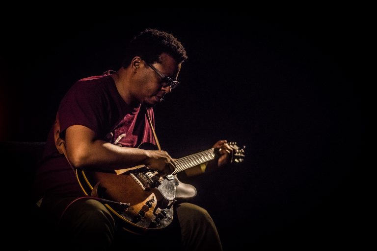 Een muzikant speelt op een elektrische gitaar in een intieme lichtsetting.