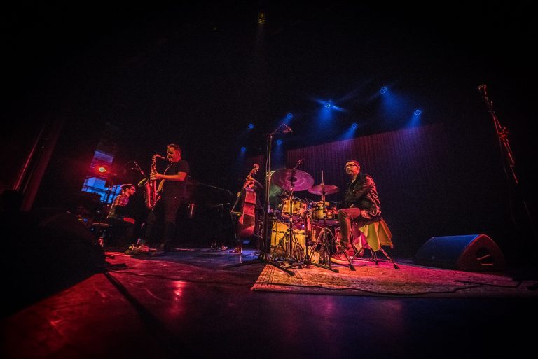 Een muziekband speelt live op een podium, omringd door sfeervolle verlichting.