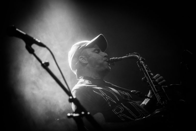 Een muzikant speelt saxofon op het podium, belicht door een sterke lichtstraal.