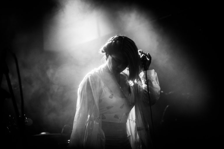 Een silhouet van een zangeres met een microfoon, omgeven door mist en zachte verlichting.