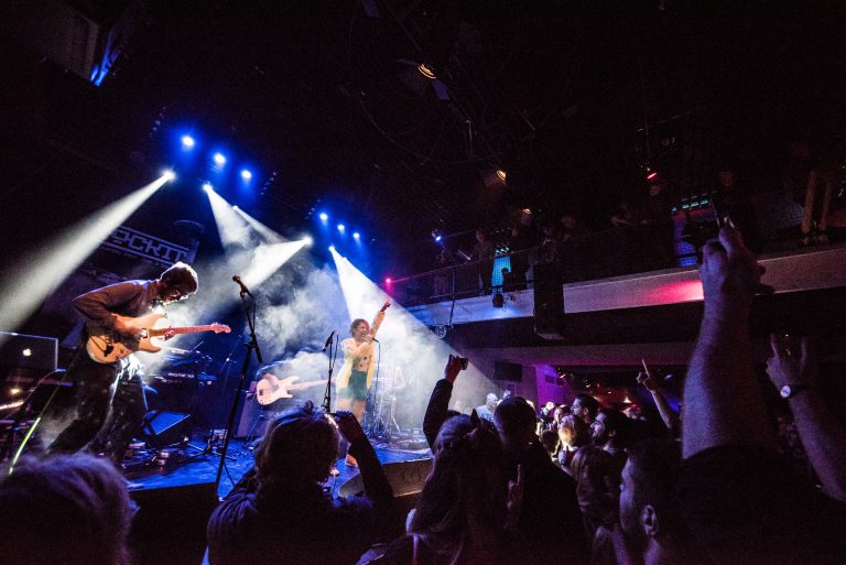 Een live optreden op een podium met lichtstralen en een enthousiast publiek.