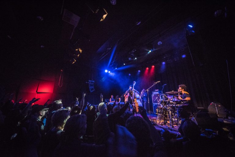 Een druk bezocht concert met artiesten op het podium en publiek dat enthousiast meedeed.
