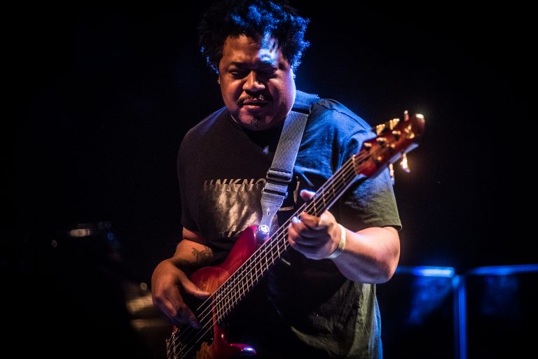 Een muzikant speelt een elektrische basgitaar op het podium, verlicht door sfeervolle lichten.