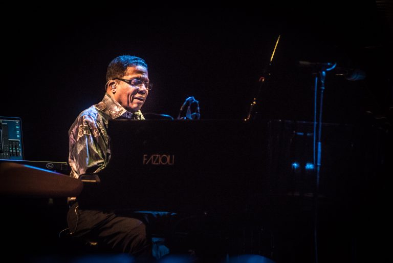 Een pianist speelt op een zwart grand piano, omringd door een sfeervolle blauwe verlichting.