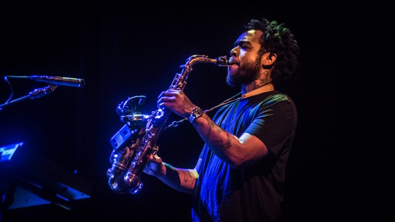 Een muzikant speelt saxofon op een podium met blauwe verlichting.