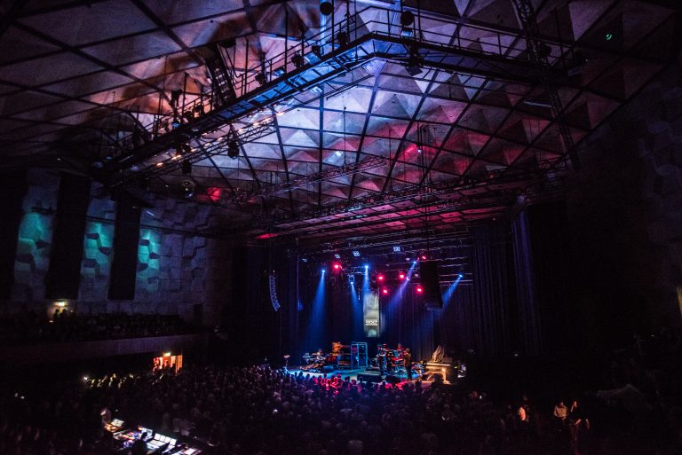 Een gebouw met een groot podium, verlicht door kleurrijke lichten, met een menigte aan de onderkant.