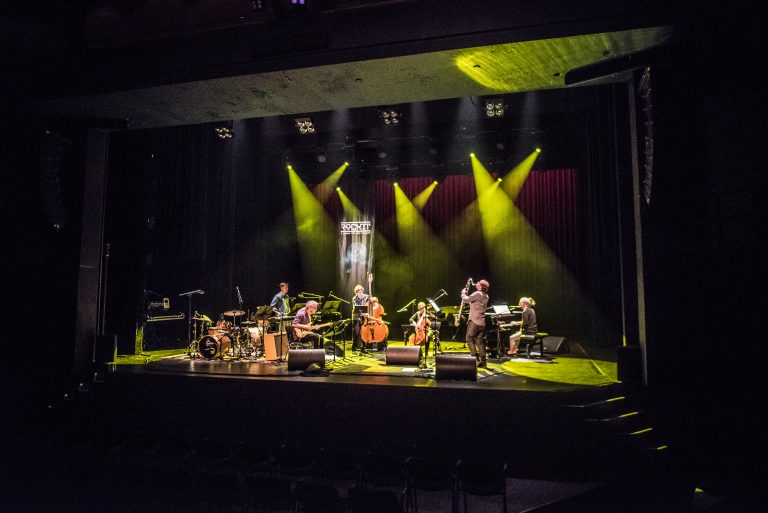 Een muziekoptreden op een podium met verschillende muzikanten en groene en gele verlichting.