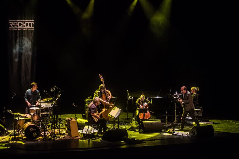 Een groep muzikanten speelt op een podium met groene verlichting.