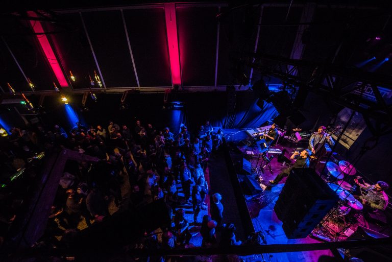 Een druk concert met kleurrijke verlichting en een publiek dat geniet van de muziek.