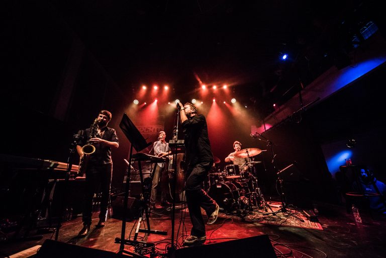 Een muzikale band optredend op een podium met kleurrijke lichten.