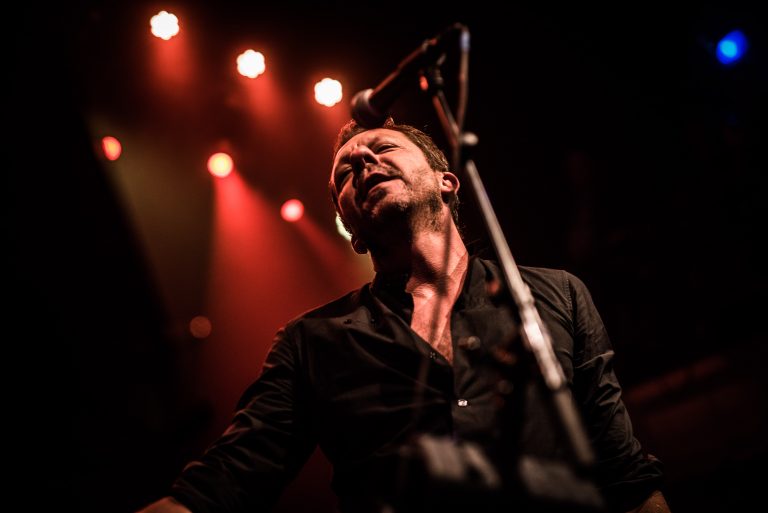 Een muzikant zingt in een gevuld podium met verfijnd lichtspel op de achtergrond.