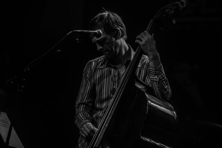 Een muzikant speelt een contrabas terwijl hij zich concentreert, met een microfoon in de buurt.