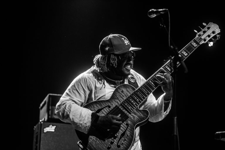 Een muzikant speelt een elektrische gitaar op het podium in een zwart-witfoto.