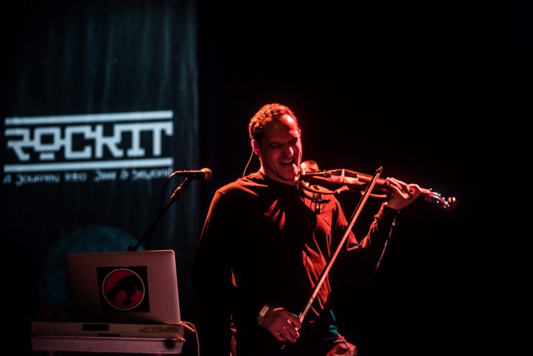 Een muzikant speelt viool op het podium met een microfoon en verlichting op de achtergrond.