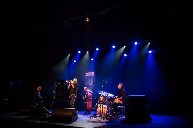 Een live jazzband speelt op een podium, verlicht door blauwe en paarse lichten.