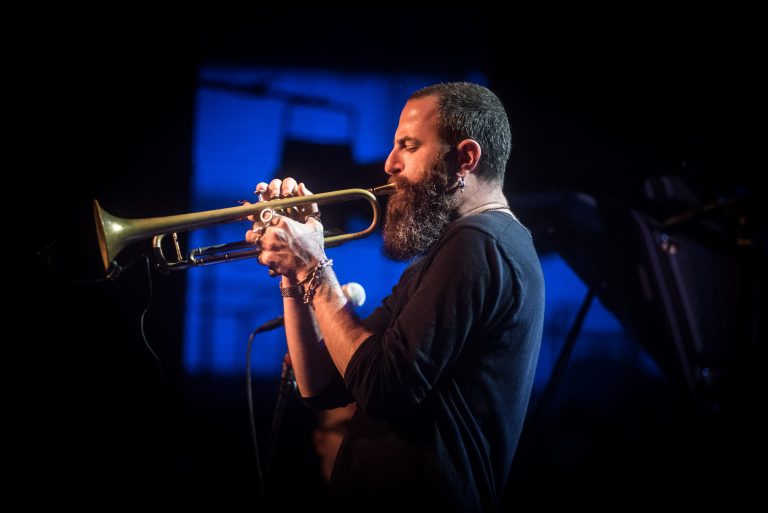 Een muzikant speelt op een trompet op het podium met een blauwe achtergrond.