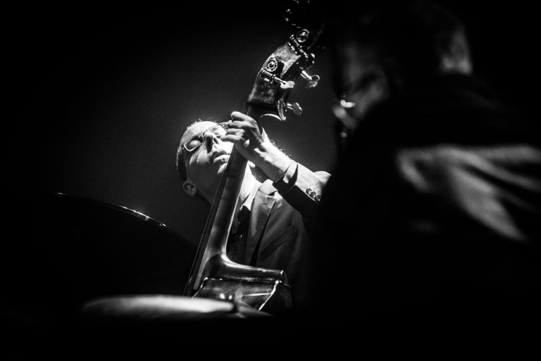 Een muzikant speelt een contrabas in een sfeervolle, zwart-wit afbeelding.