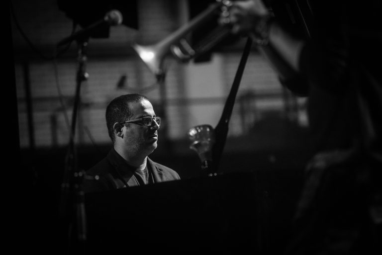 Een pianist speelt in een donkere setting met focus op zijn gezicht en handen.