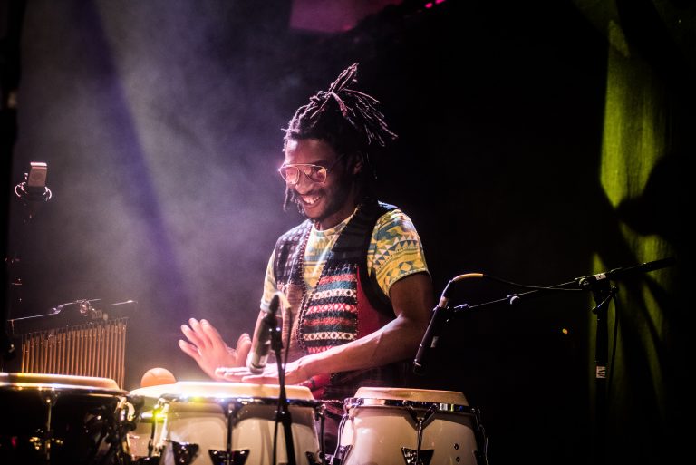 Een muzikant speelt vrolijk op conga's in een sfeervol verlichte omgeving.