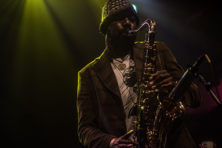Een muzikant speelt saxofon op het podium, belicht door groene en gele lichten.