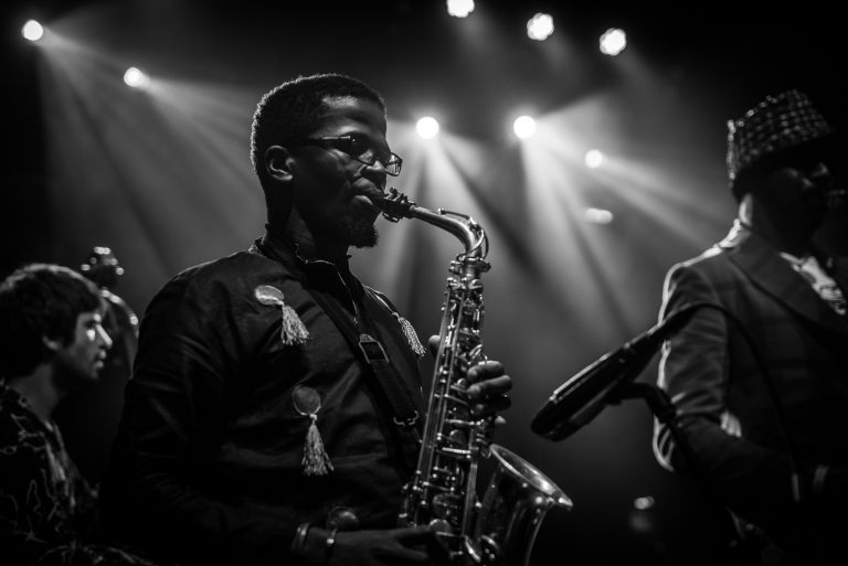 Een muzikant speelt saxofoon op een podium met sfeerverlichting in zwart-wit.