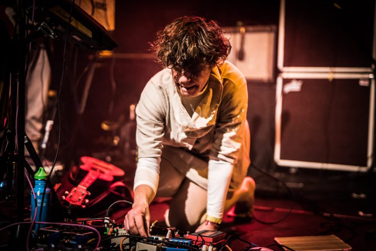 Een muzikant knielt op het podium terwijl hij met apparatuur en effecten speelt.