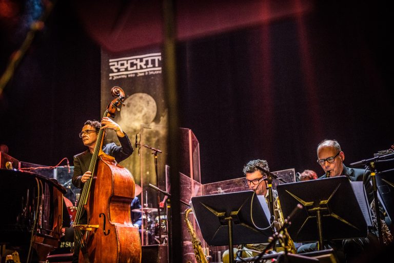 Een jazzensemble speelt op het podium met verschillende instrumenten, waaronder een contrabas en saxofoon.