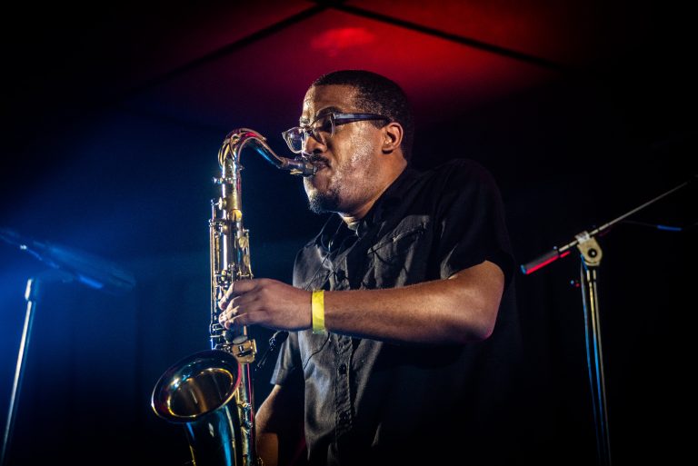 Een muzikant speelt saxofon op een podium met opvallende verlichting.