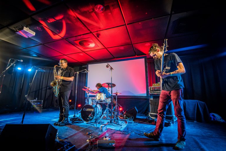 Een band voert live muziek uit op het podium met kleurrijke verlichting.